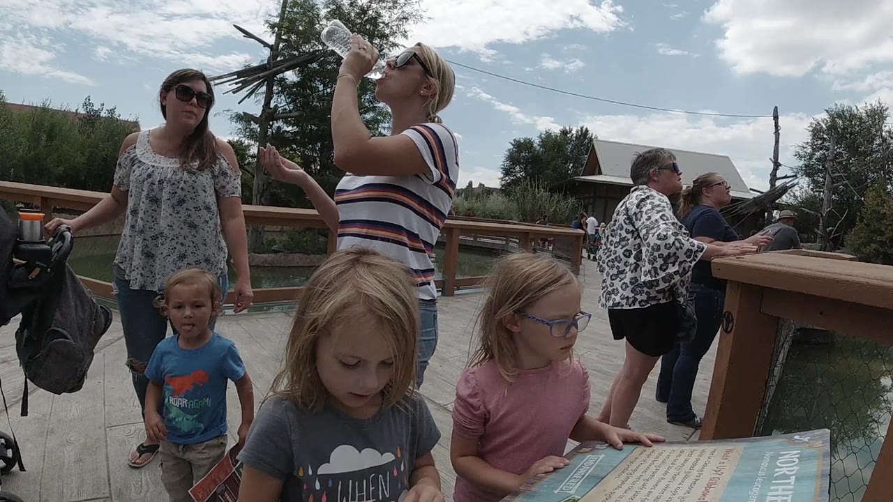 Children and adults near an outdoor zoo information board.