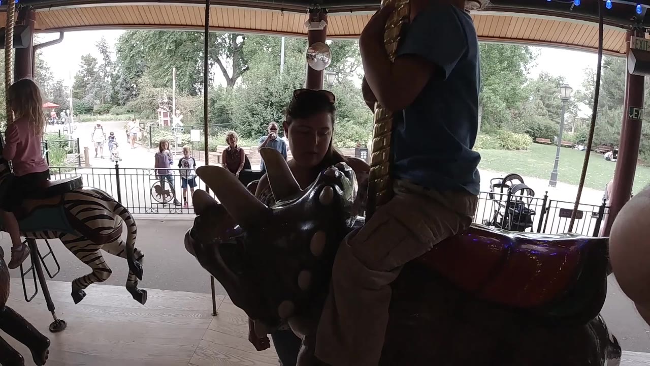 Carousel animal in shadow with child rider and adult nearby.
