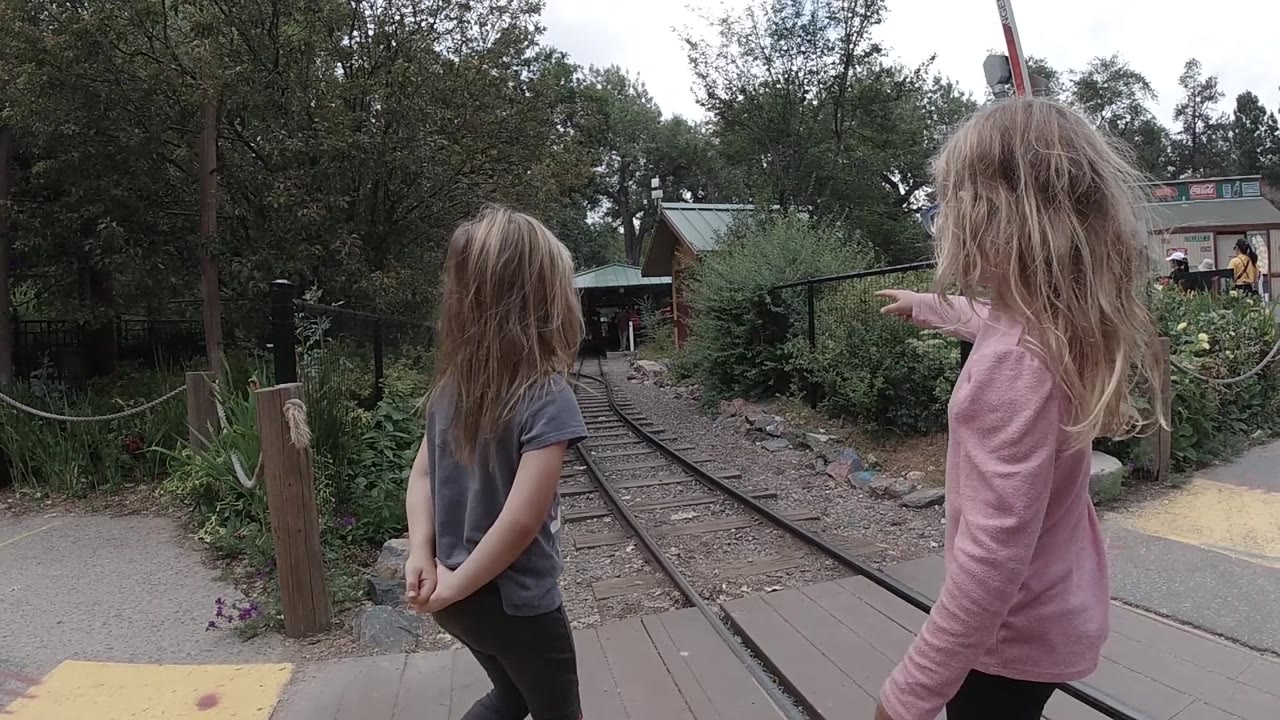 Two girls wait beside a track crossing in a wooded zoo area.