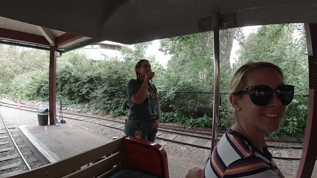 Foreground woman smiles beside the open train car with rails outside.