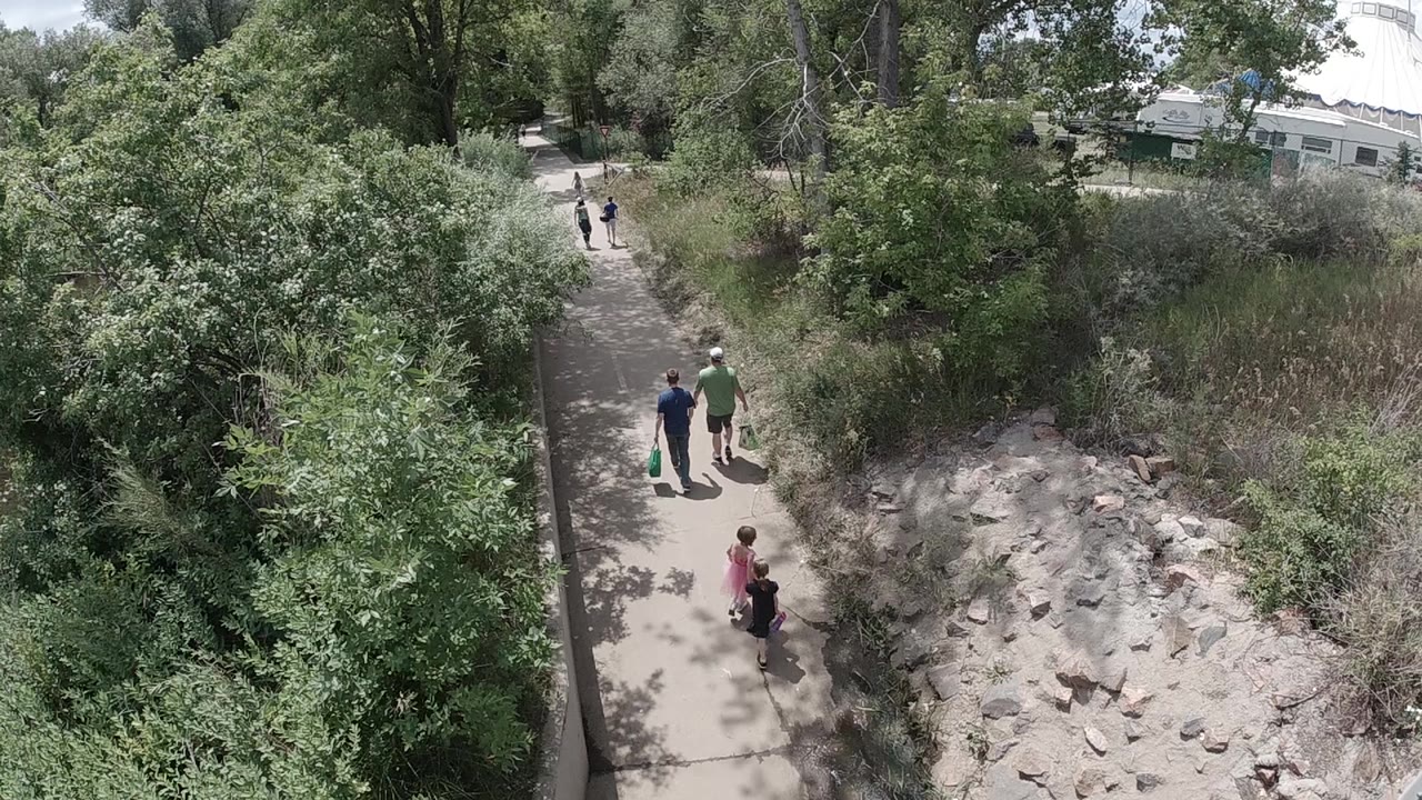 Elevated Colorado view of people on a narrow paved walkway with leafy trees to the left and dry rocks and brush to the right.