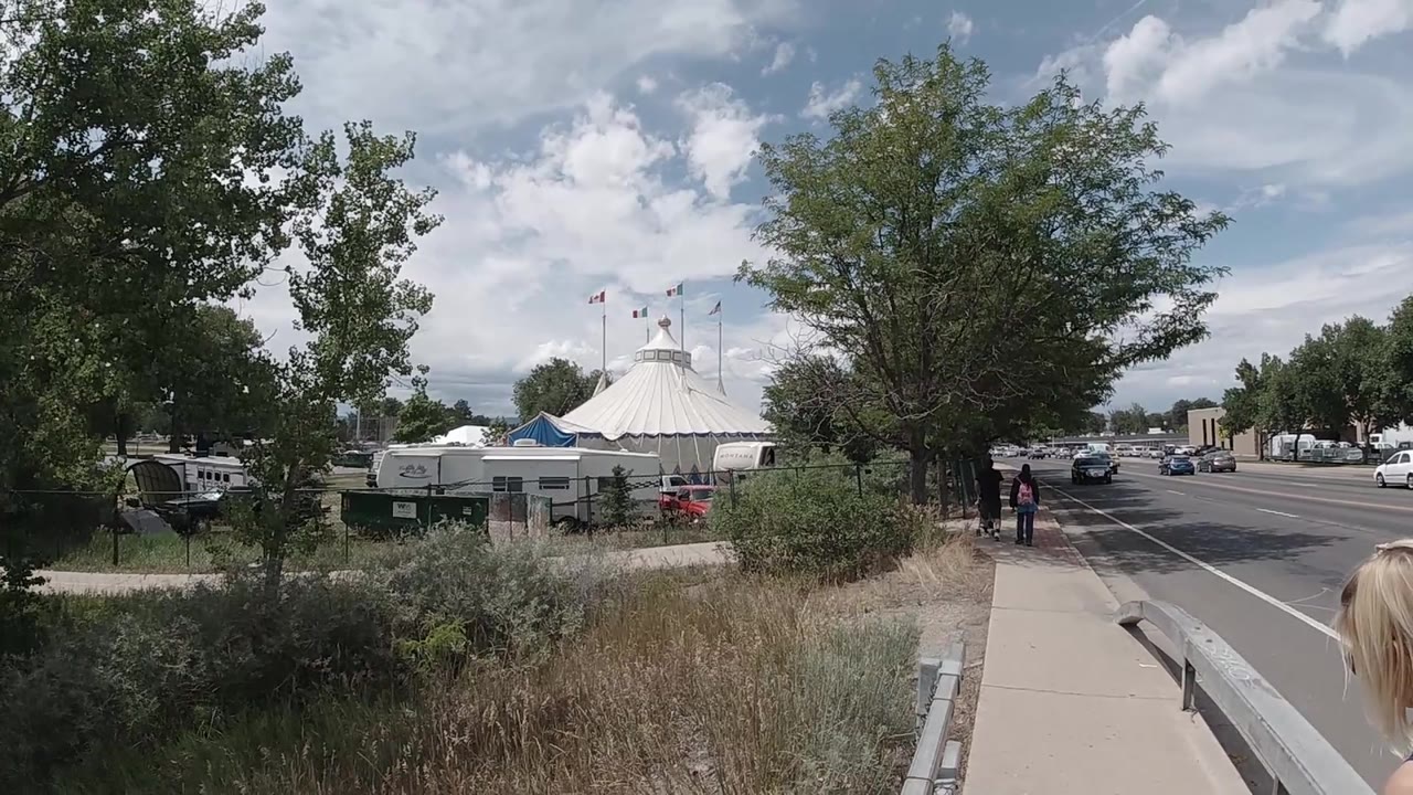 Roadside sidewalk with tent, trees, and distant pedestrians.