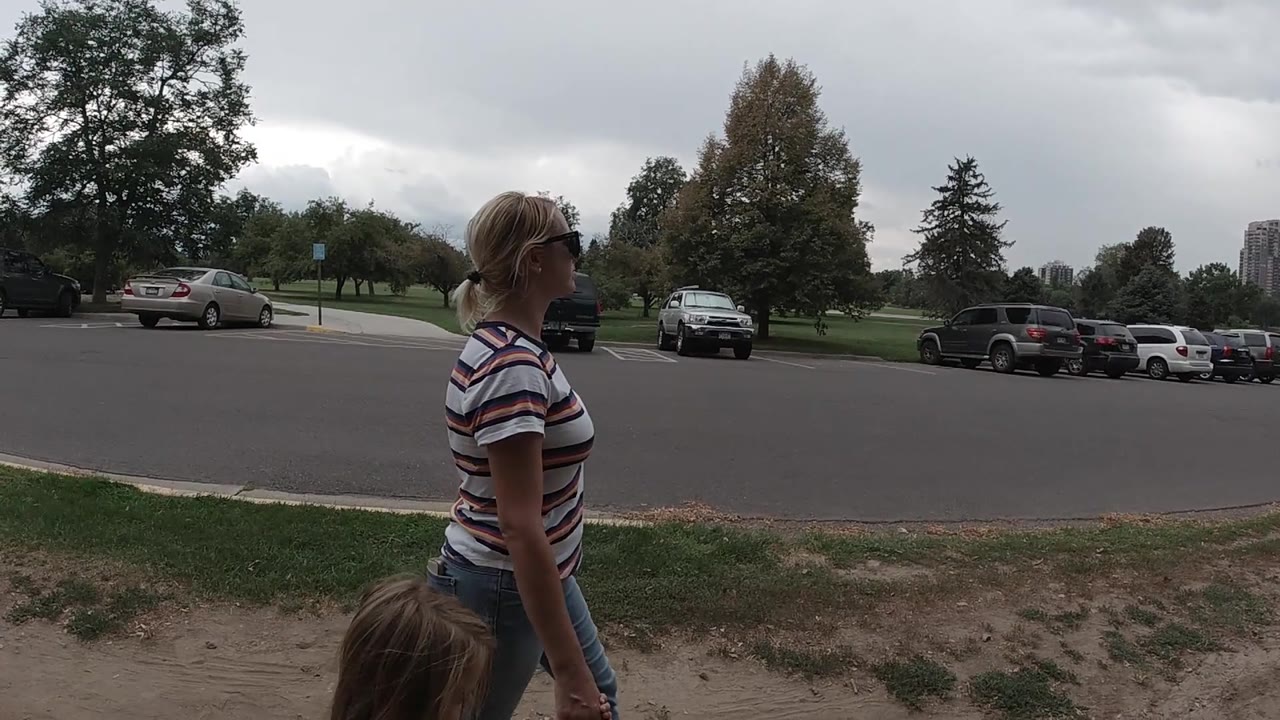 The pair advances slightly to the right of frame, with the woman holding a small water bottle and the child partly cropped below her in a Colorado park setting.