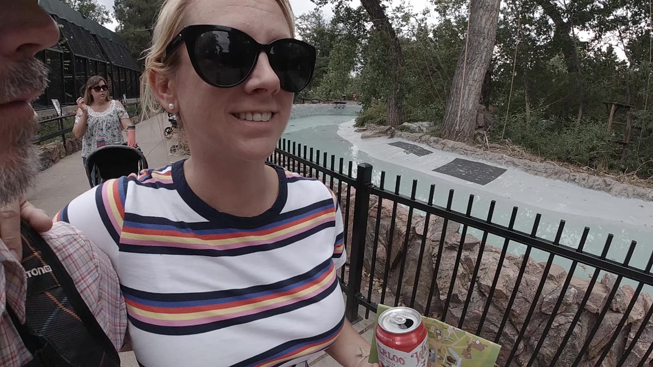 The woman remains close to the lens while a black fence and curving zoo path in Colorado stretch behind her under muted daylight.