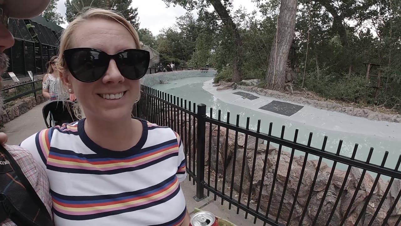 Woman smiling directly near black fence at zoo.