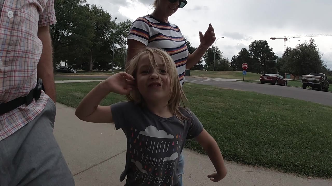 Girl gestures upward while walking between two adults.