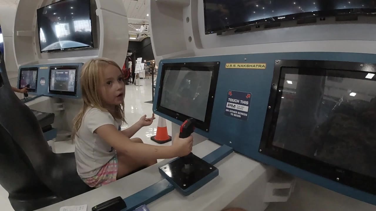 Child seated beside blue interactive exhibit panels.