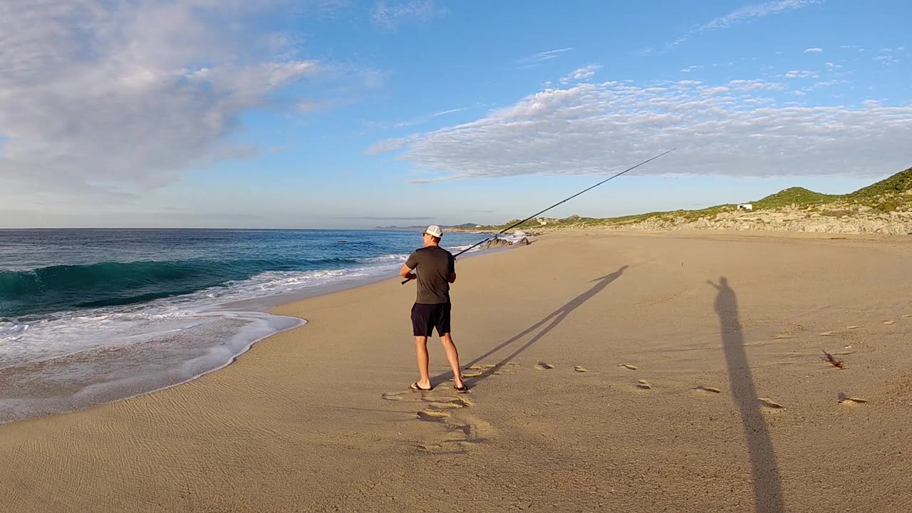 Man with fishing rod on a sandy beach beside surf