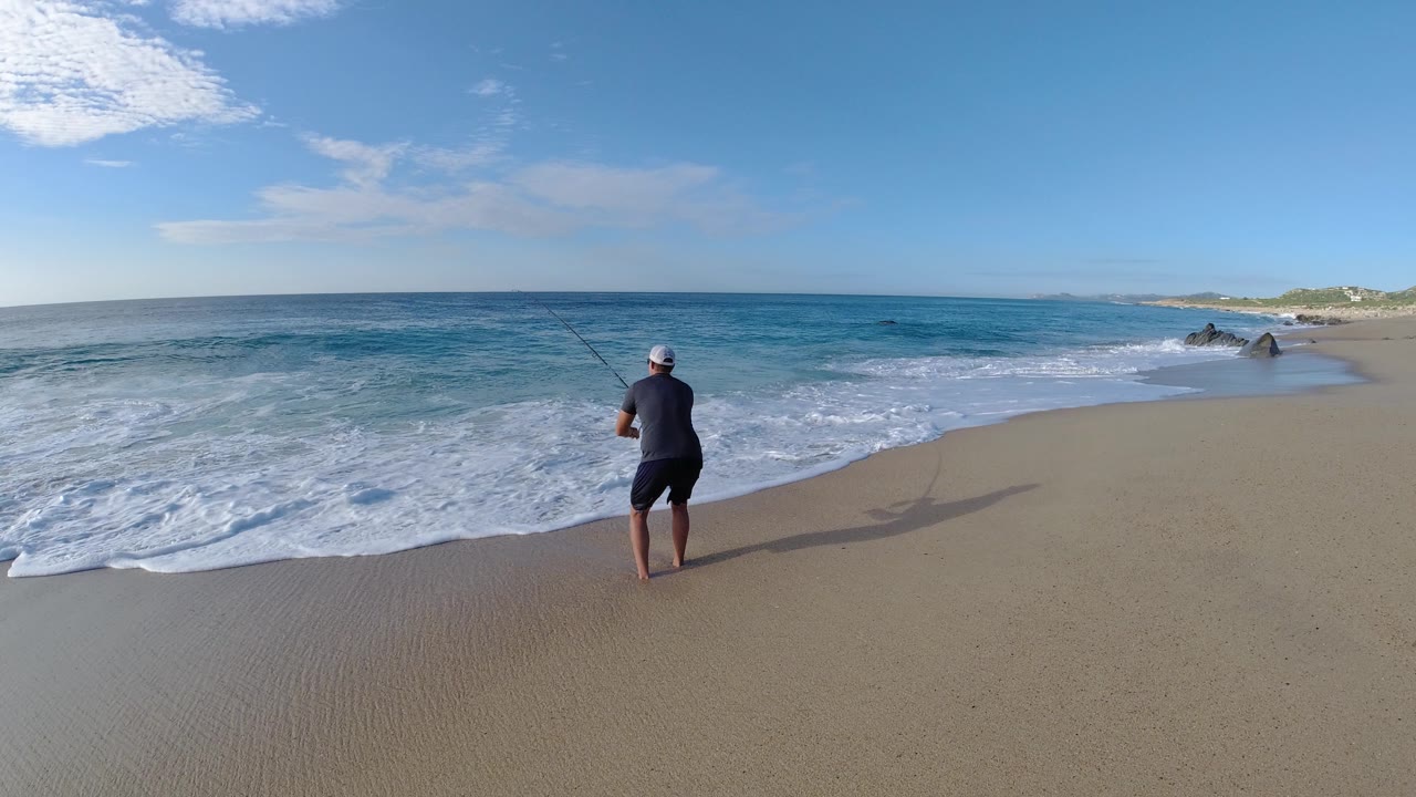 Man stands near the surf on a sandy beach with ocean ahead.