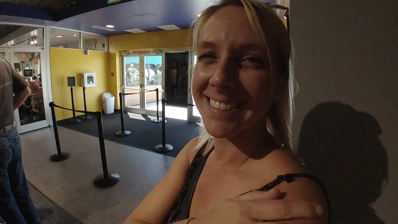 Blonde woman smiling near an indoor entrance lobby.