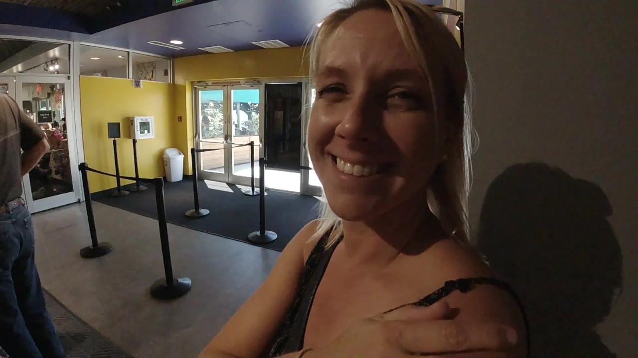 The woman remains close to the lens and smiles in the Colorado lobby while the glass entry doors and stanchion line stay clear in the background.