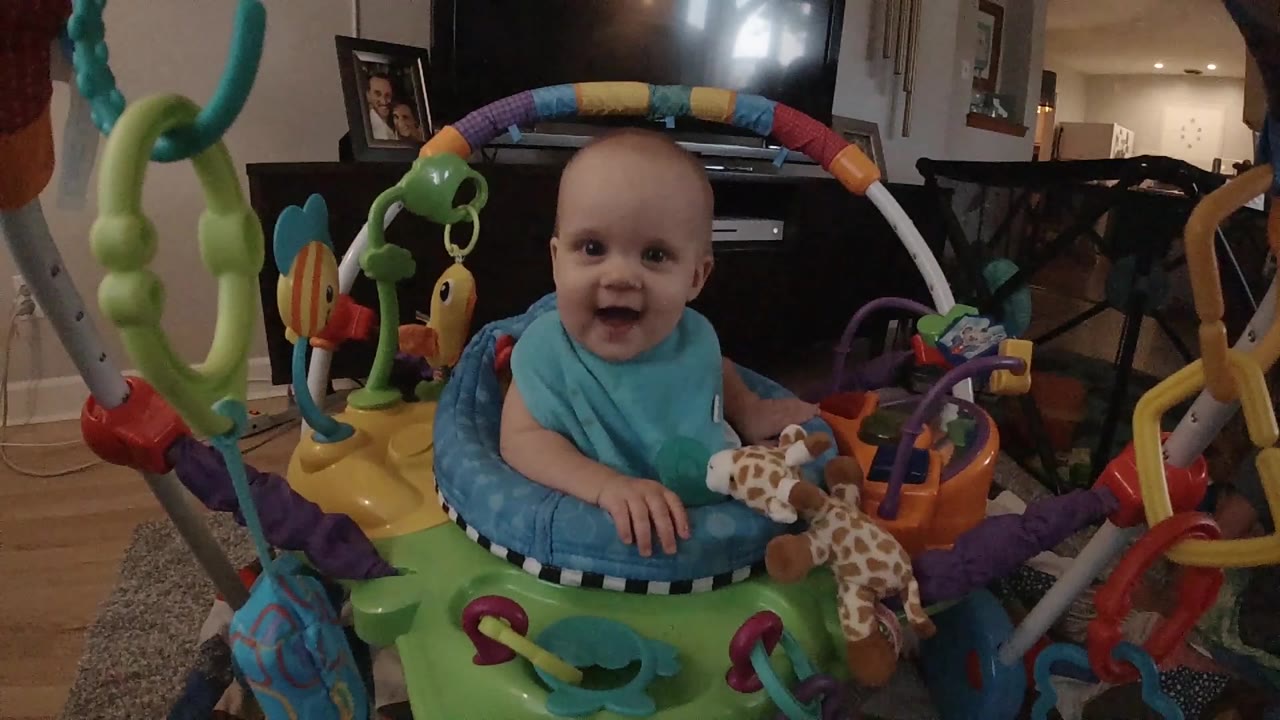 Baby smiles from inside a green jumper with toy arches around them.