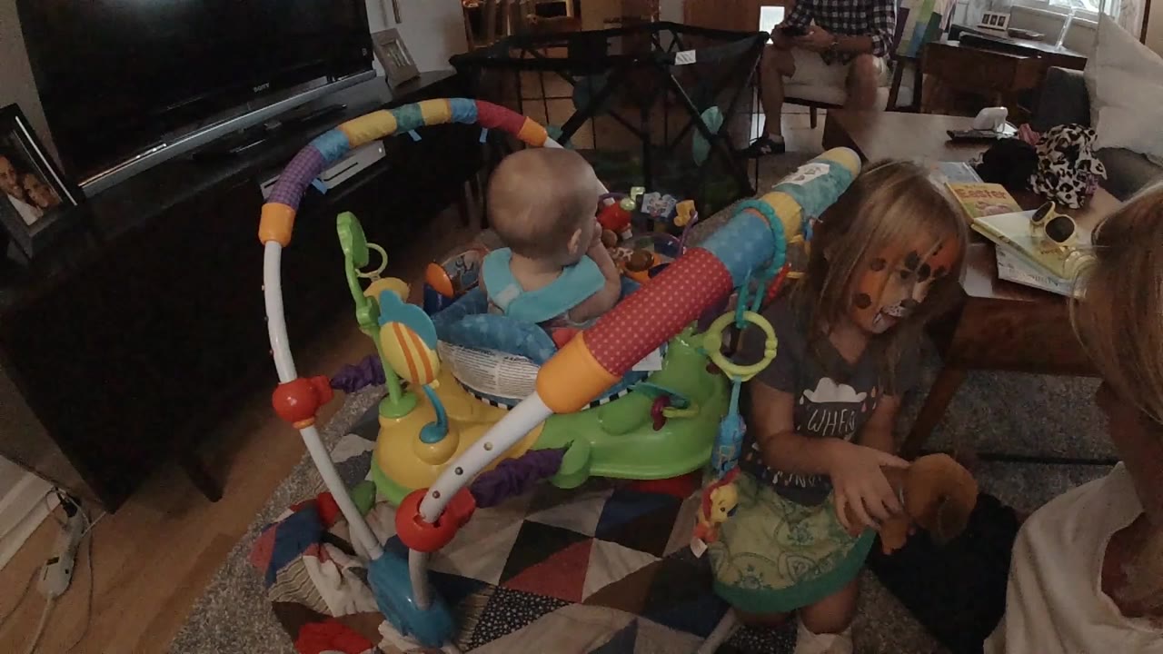 Baby faces away in jumper as girl stands beside toys.