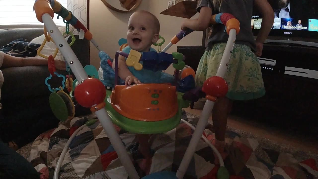 Baby in a colorful jumper faces slightly left in a living room.