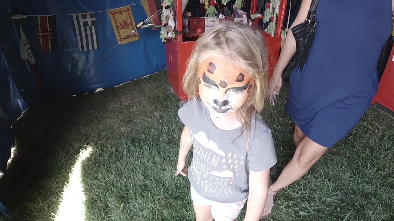 Face-painted girl looking up near blue tent fabric