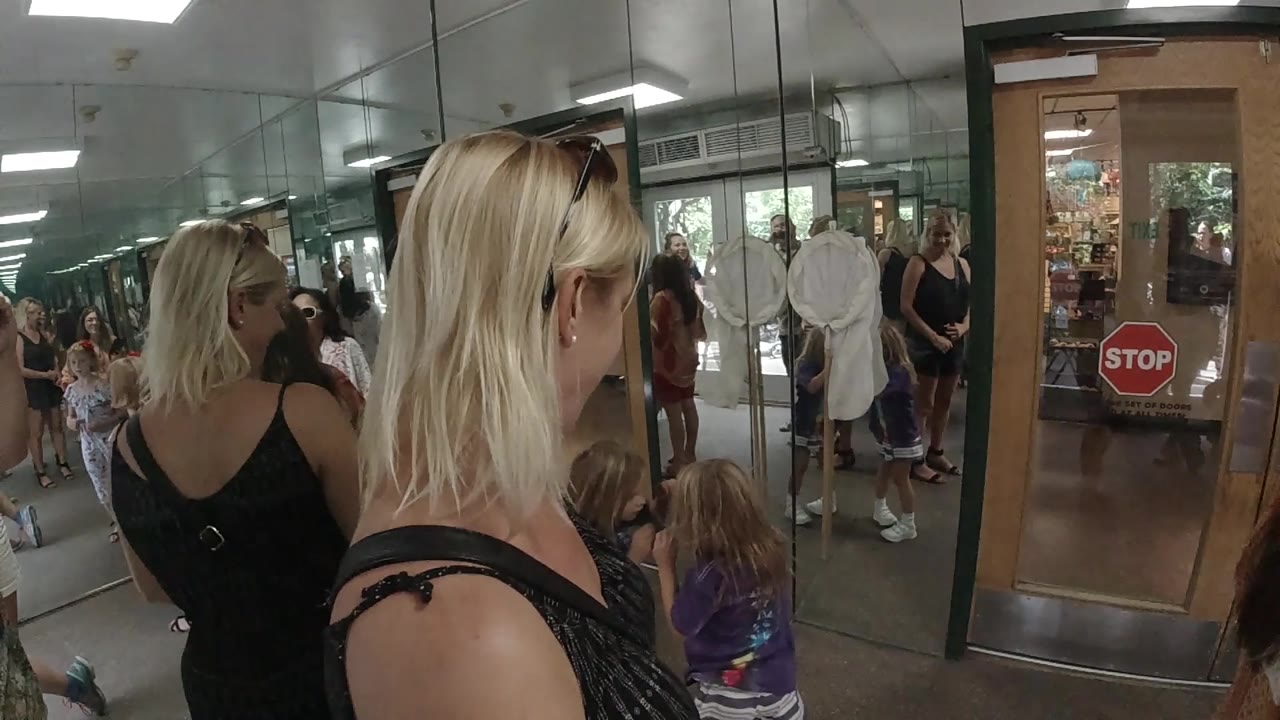 A close side view shows the blonde woman with sunglasses on her head beside a young girl, with other people gathered near the glass doors in Colorado, United States.