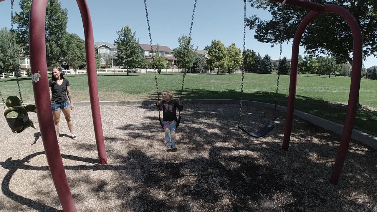 Young girl on a playground swing with an adult standing nearby.