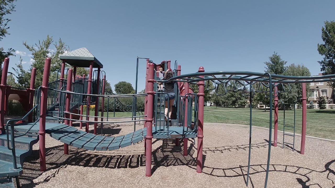 The Colorado playground remains framed wide as a child stands near the central platform beside red posts and teal railings.
