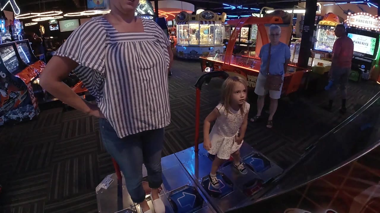 In Denver, the woman stands with one hand on her hip as the little girl looks across the arcade floor near the dance game rails.