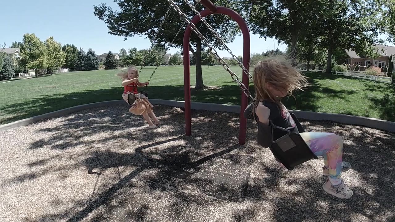 Two girls on playground swings under tree shade
