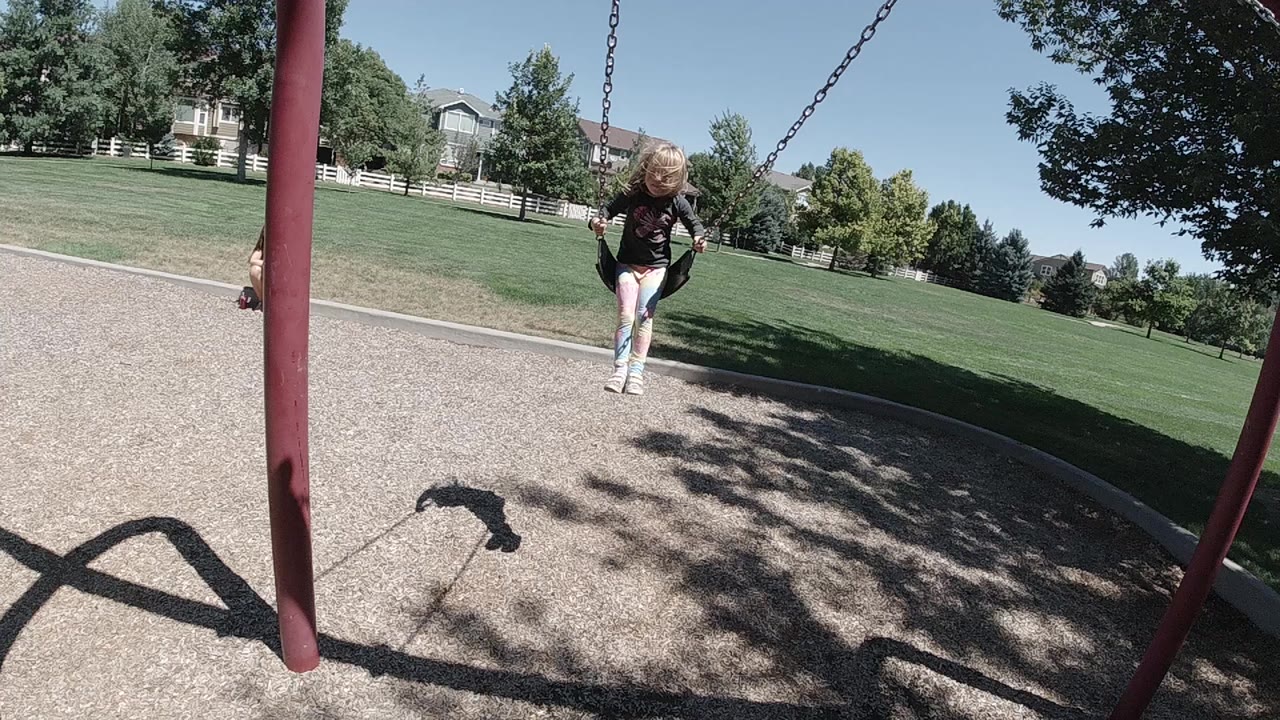 Blonde child swings toward the camera on a playground swing.
