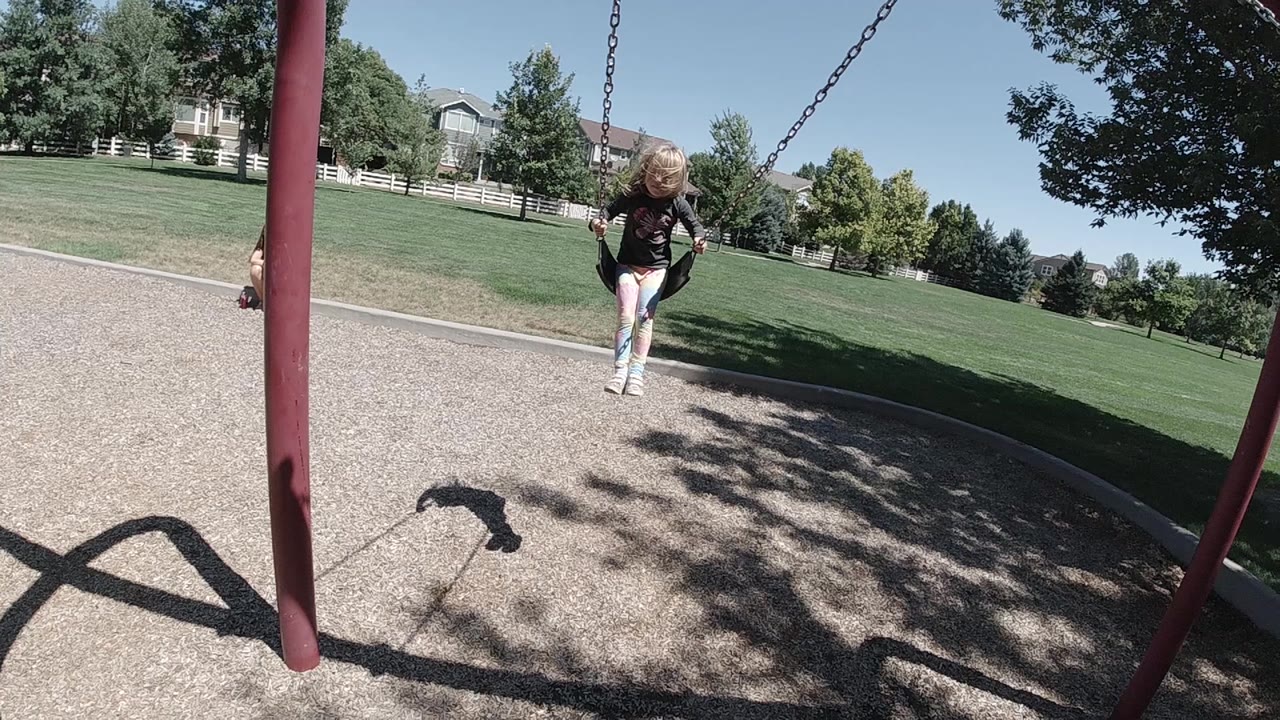The child rides forward on the swing with a red support post on the left and the sunny Denver lawn stretching behind.