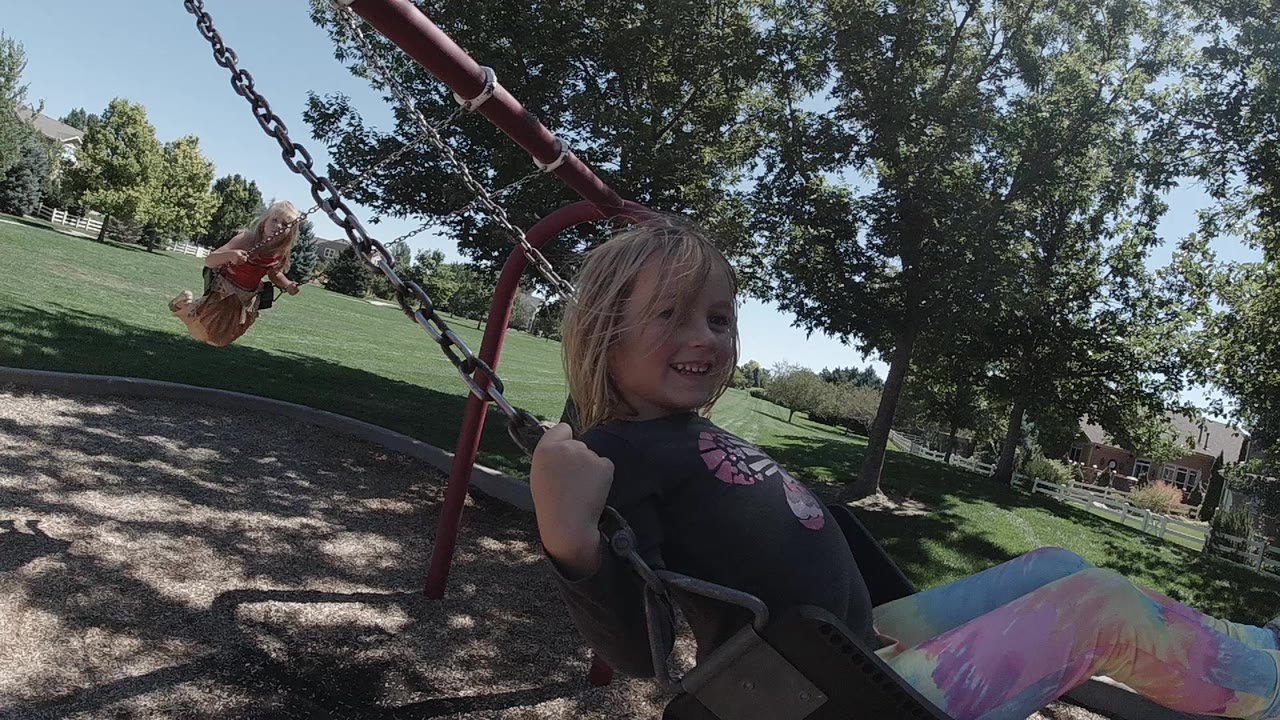 Girl in a swing seat smiling near a red swing set.