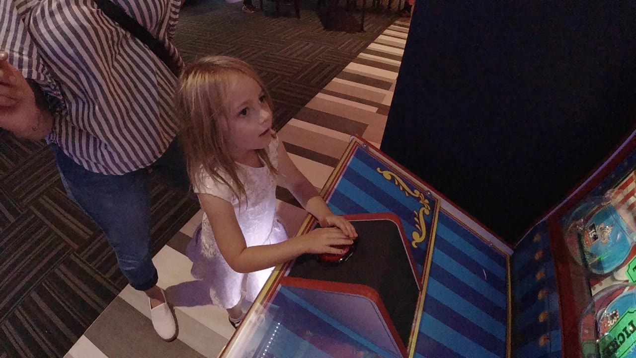 Young girl at an arcade game with an adult standing beside her.