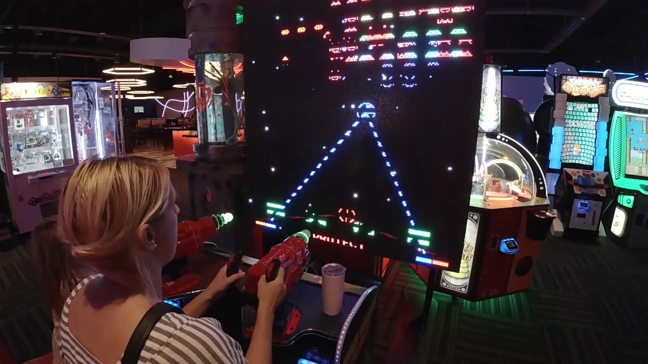 Galaga screen with blue attack path in front of woman.