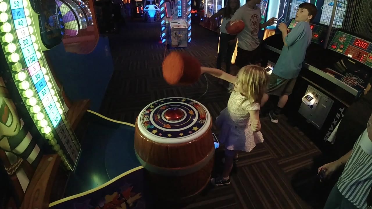 At the start of the Denver arcade clip, a young girl leans toward a barrel-shaped hammer game as a red mallet moves over the round target.