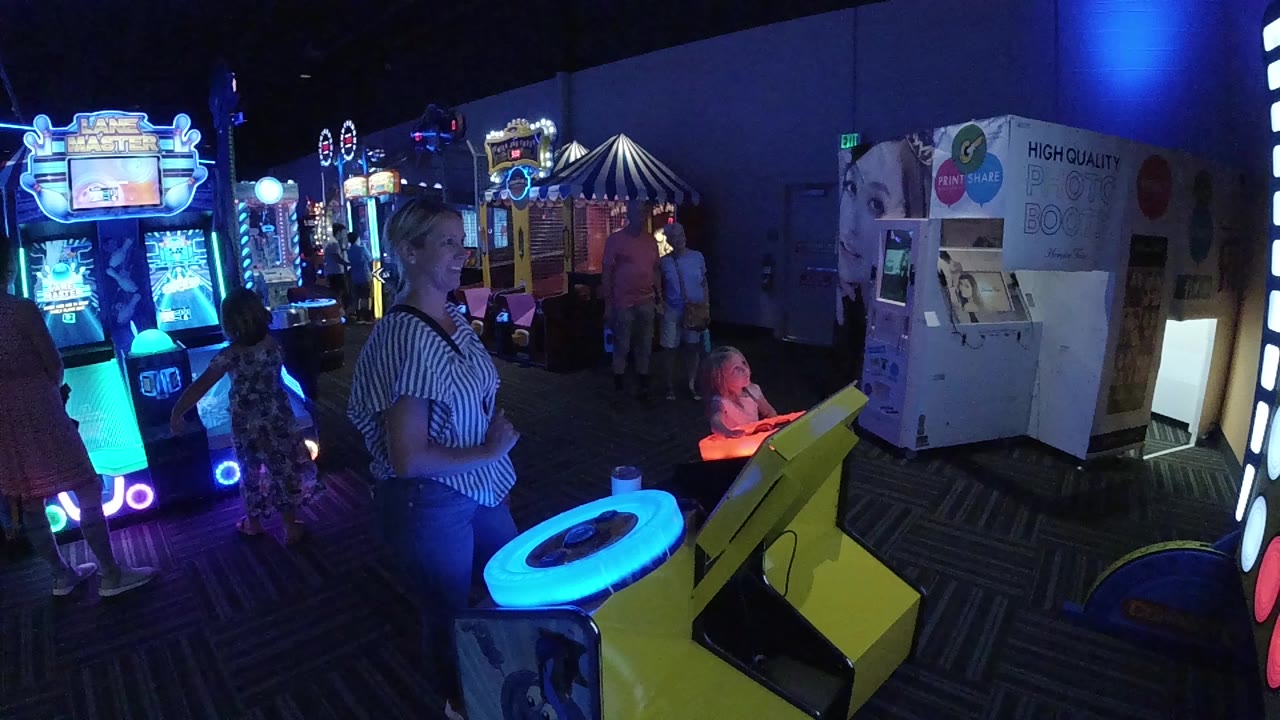 Wide arcade scene with a woman, child, neon machines, and glowing blue game table.