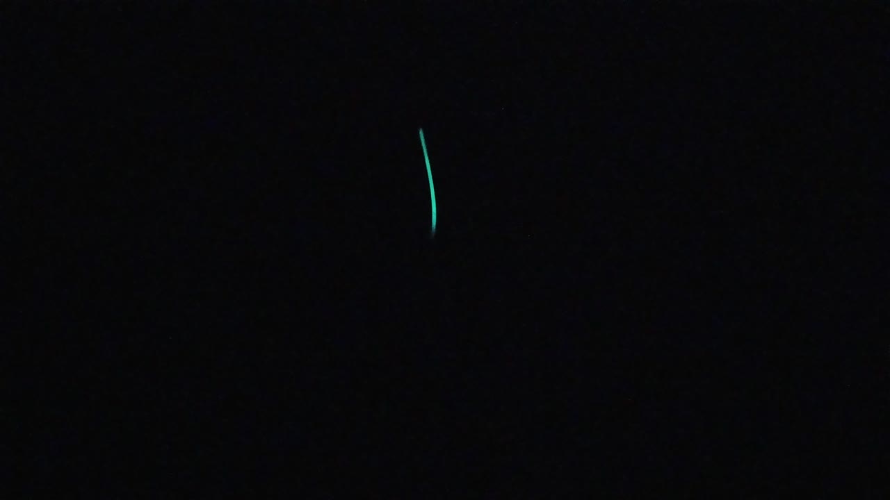 Near-black frame with two or three small teal-green luminescent streaks distributed toward the left side; no visible people in this frame.