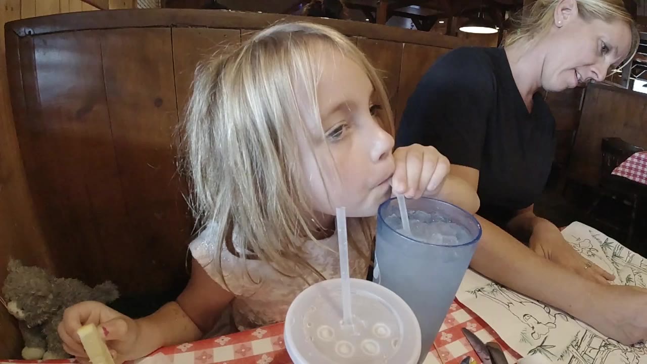 At the start of the Colorado clip, a blonde young girl sips from a blue plastic cup while an adult woman sits partly visible behind her.