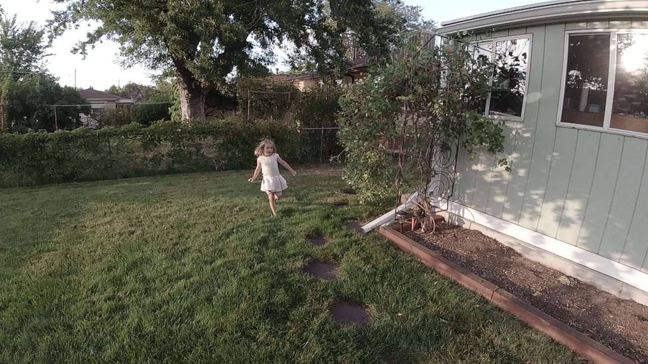 Young girl running across grass near a pale building.
