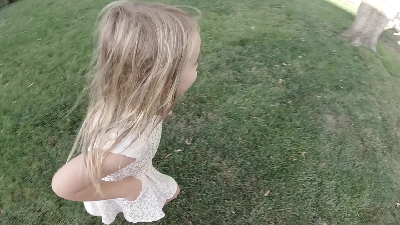 The child runs farther across the lawn, turning slightly away as a tree trunk and sidewalk begin to appear near the upper right of the frame.