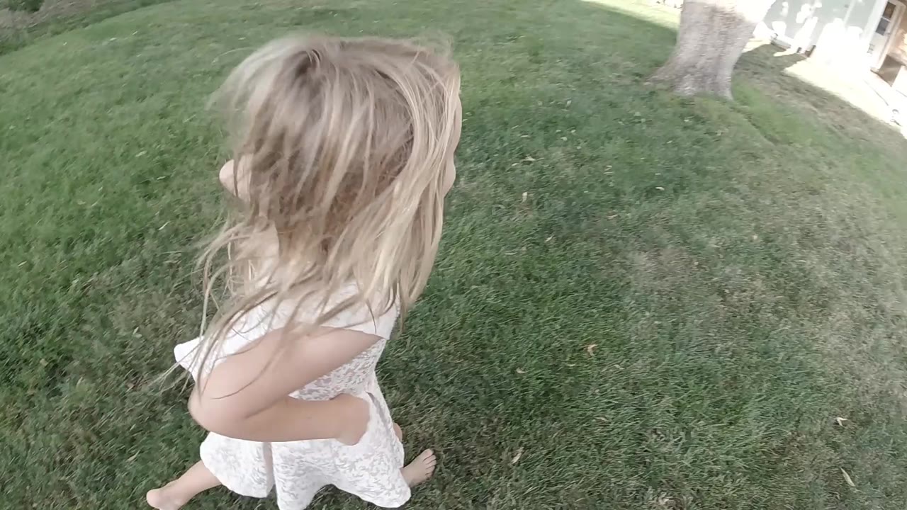 Girl running on grass near a tree and sidewalk