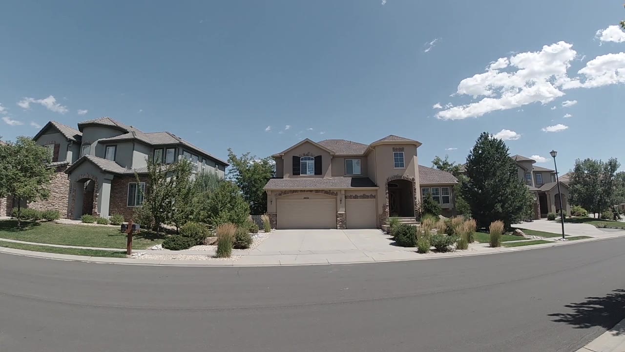Wide Colorado residential exterior with two neighboring homes, pale driveway concrete, landscaping, and a bright cloud cluster overhead with no visible people.