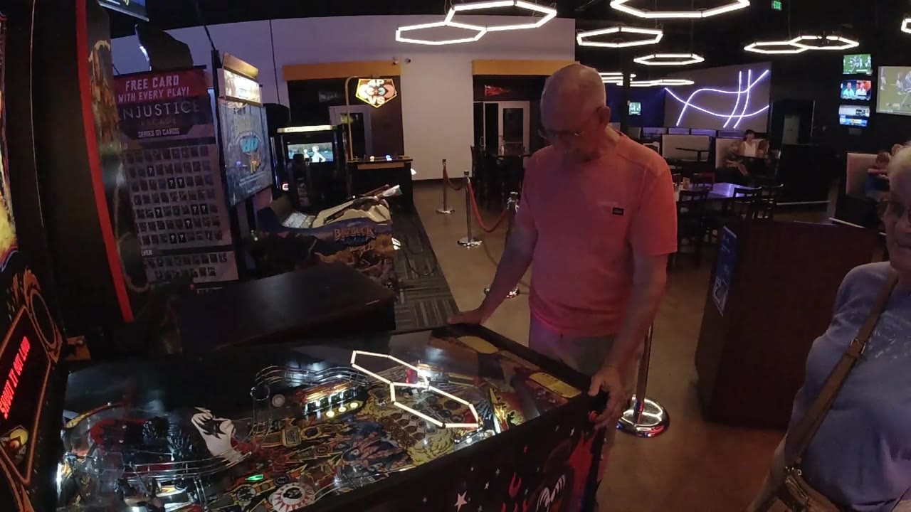 Pinball player stands beside arcade cabinets and wall lighting.