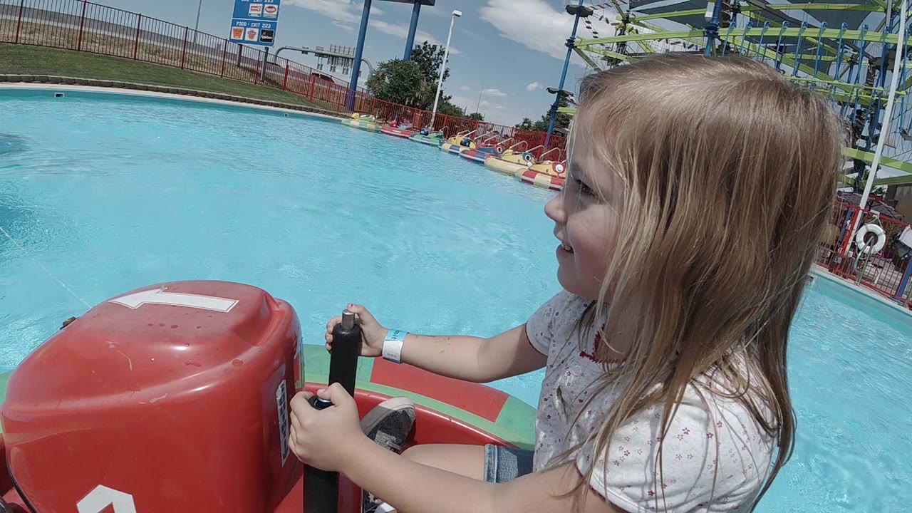 The Denver bumper boat ride continues with the girl turned toward the pool, her hands on the controls and the red bow panel filling the left foreground.