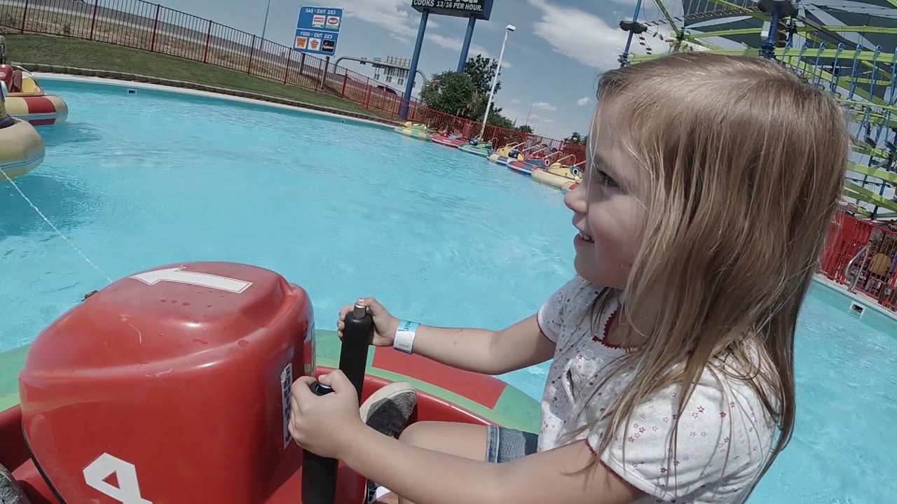 A yellow bumper boat begins to appear in the Denver pool background while the girl keeps both hands on the red boat controls in the foreground.