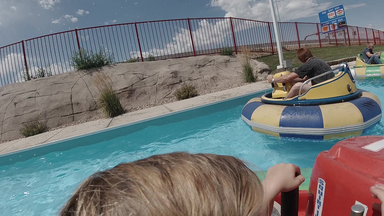 Bumper boats float beside a rock wall and red fence.