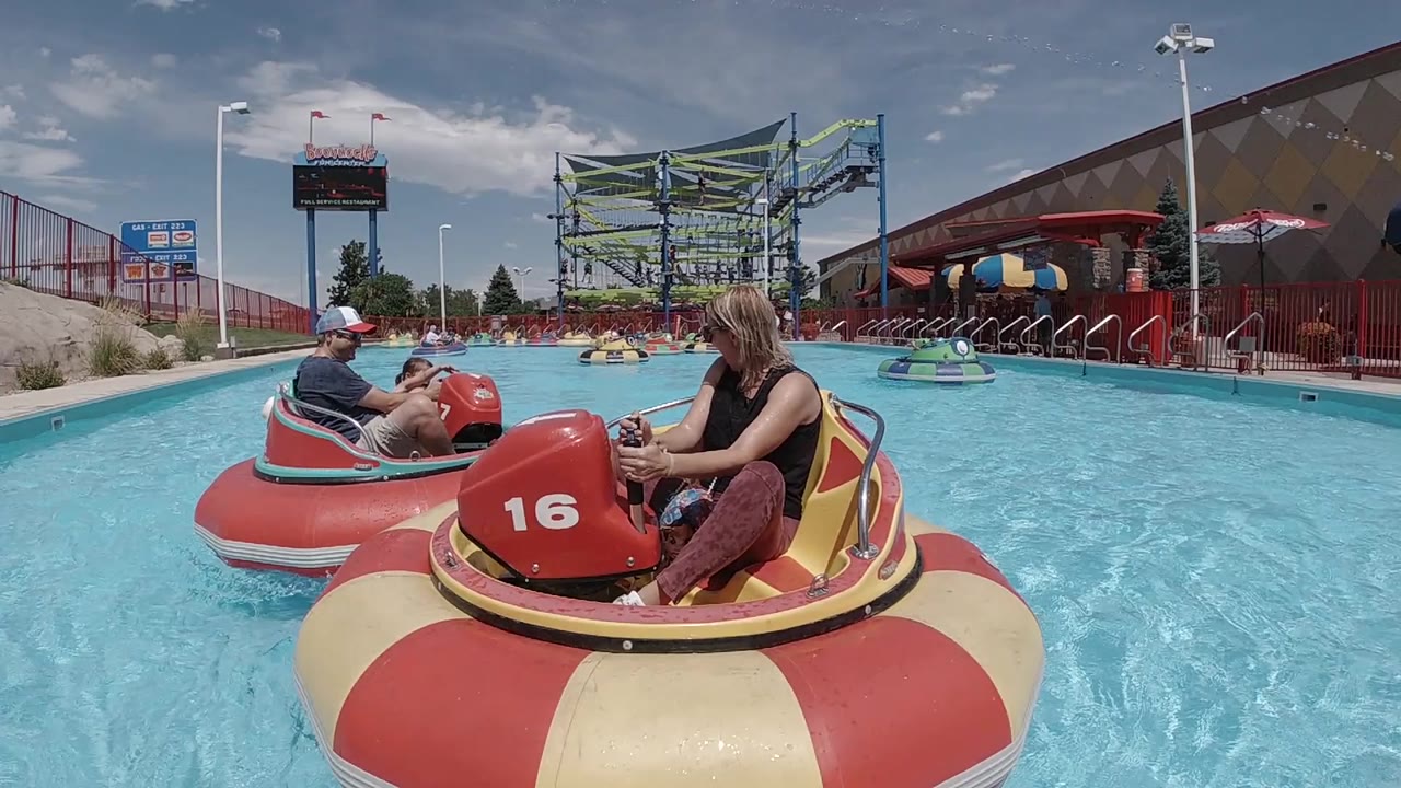 At the start of the Denver clip, a woman sits in red boat 16 on bright blue water while another rider floats ahead and park structures fill the background.