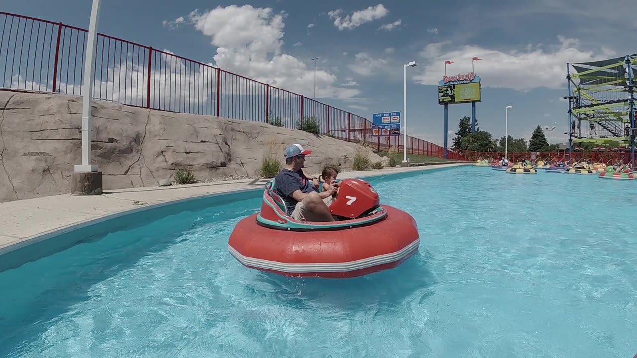 The red bumper boat remains near the wall as the adult and child face forward in the bright blue water at the Denver amusement park.