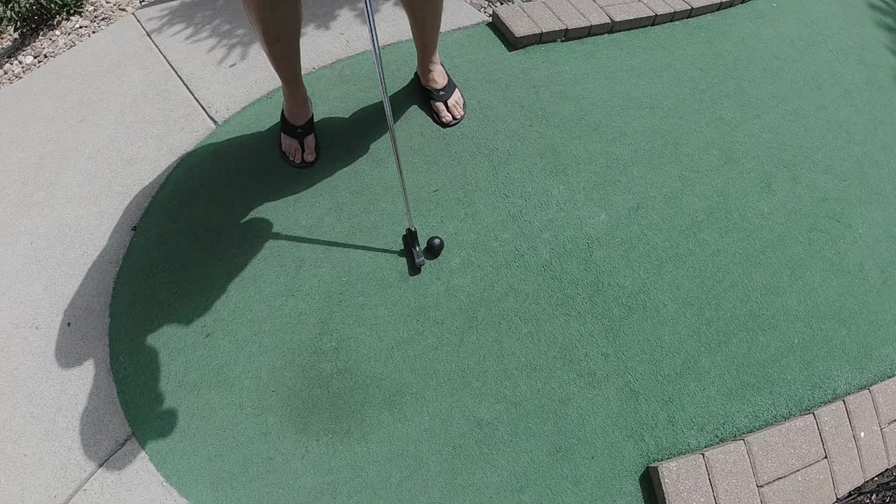 Golfer's feet, putter, and black ball on a green.