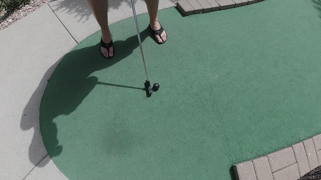 Golfer stands over a putt on a green in bright sun.