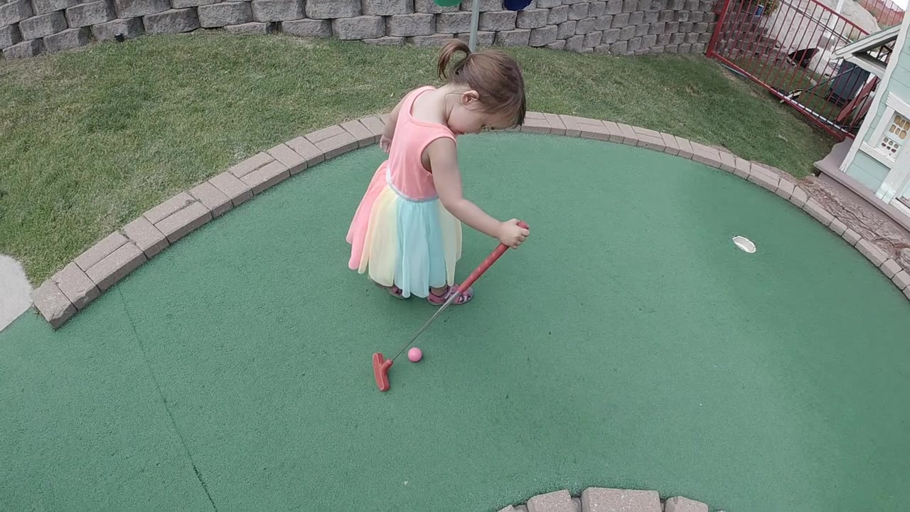 Girl drags a ball with a red putter on mini golf turf.