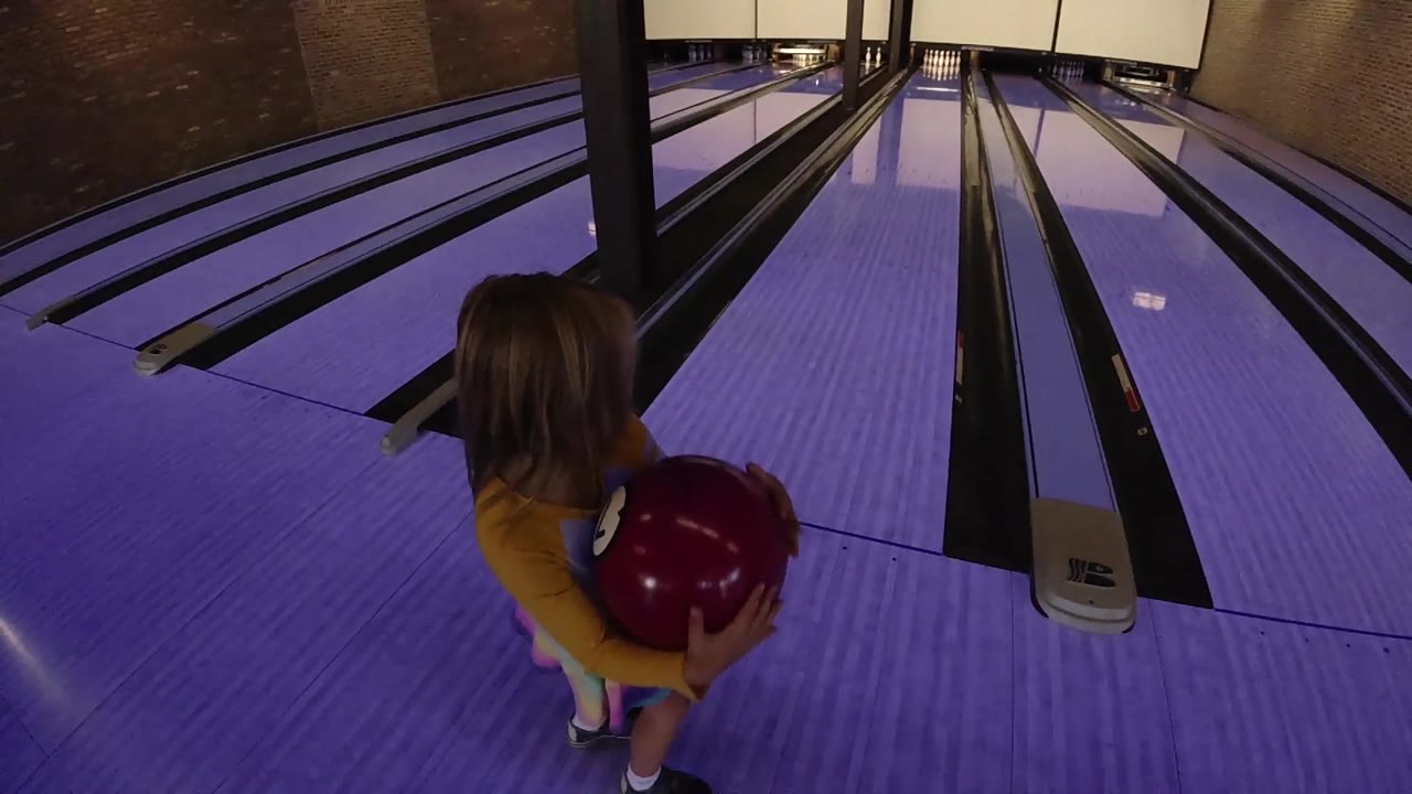 Girl shifts position while holding the red bowling ball.