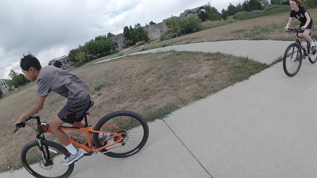 A boy on an orange bicycle rides left of center while a second boy on a dark bicycle appears at the right edge of the Denver path.