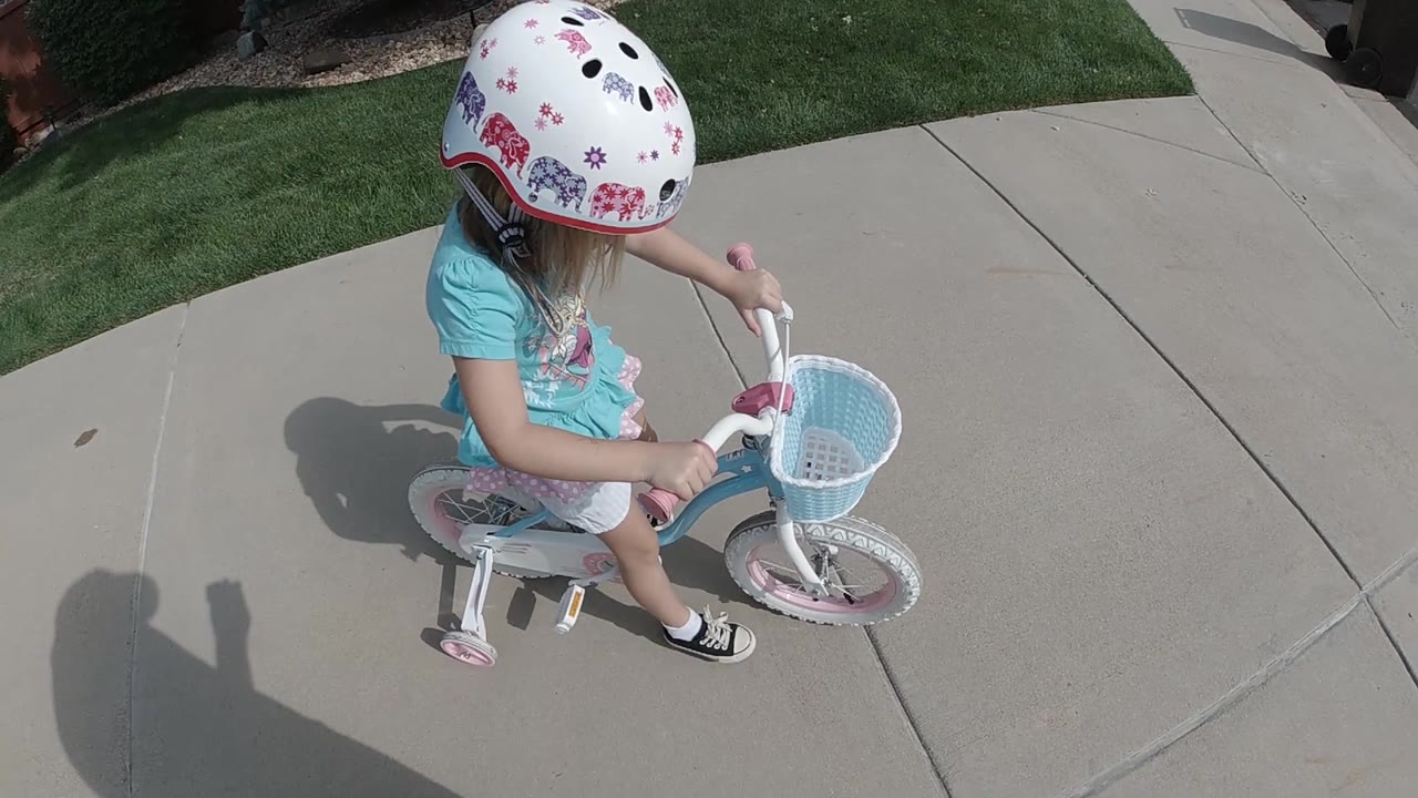 Girl on small bicycle viewed from above on a sidewalk.