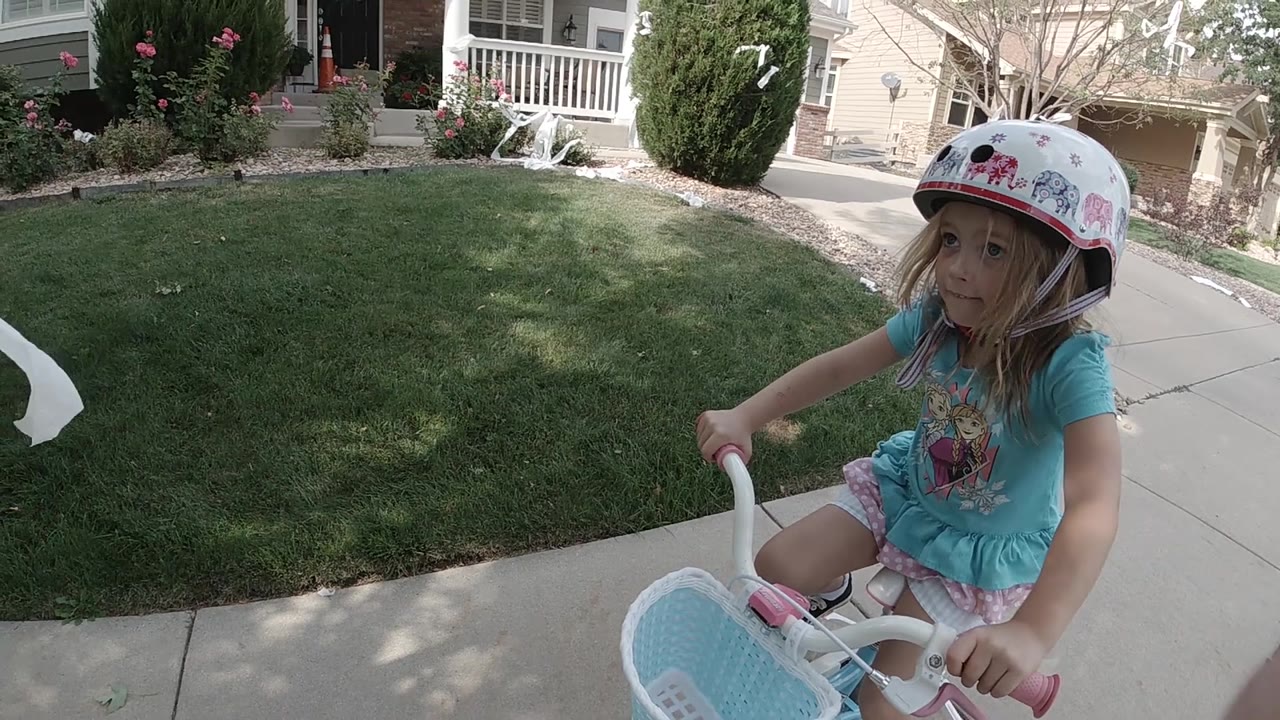Helmeted girl riding past lawn and shrubs.